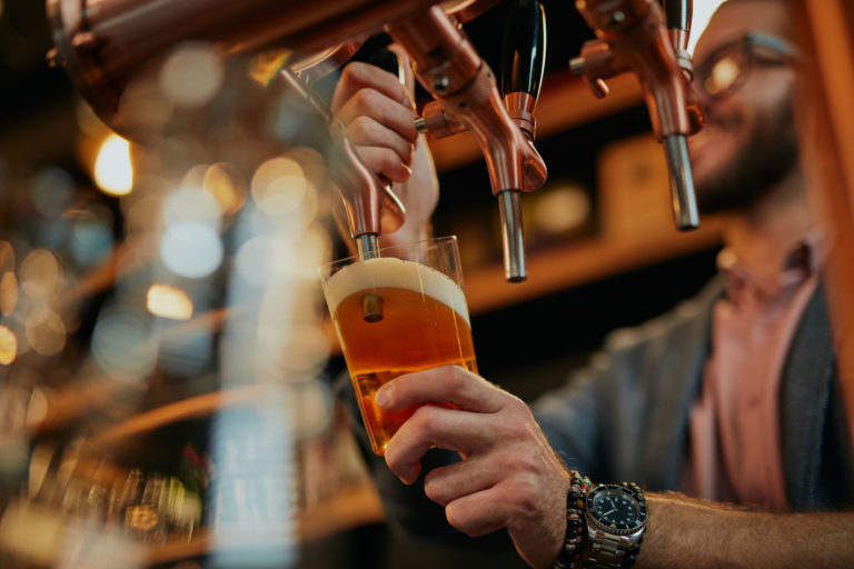 Tattooed caucasian barman pouring beer while standing in pub. Tattooed caucasian barman pouring beer while standing in pub.