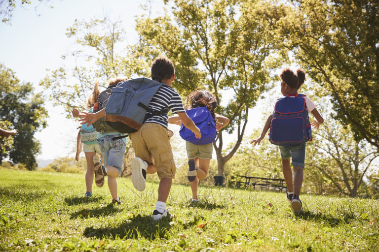 Five school kids running in a field, back view, close up